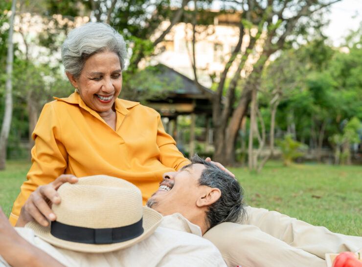 Asian senior elderly couple spend time on romantic date in the garden. Happy family, attractive mature older man and woman feel joyable and relax, having a picnic together at public park during sunset