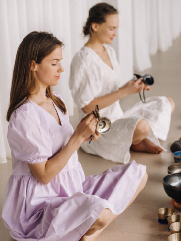 Two female yoga teachers play on Tibetan bowls in the gym during a yoga retreat.