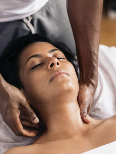 Relaxed woman lying down and receiving a neck massage. The masseuse is a handsome african american man.